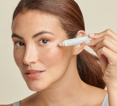 Woman applying a cosmetic product to her face with a neutral background