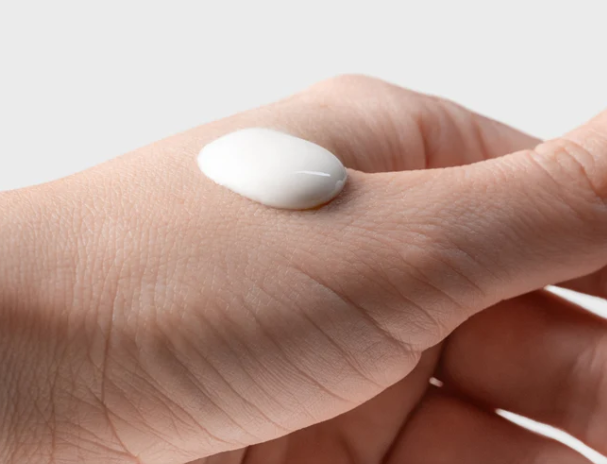 Hand with a small white sample of product on a plain background